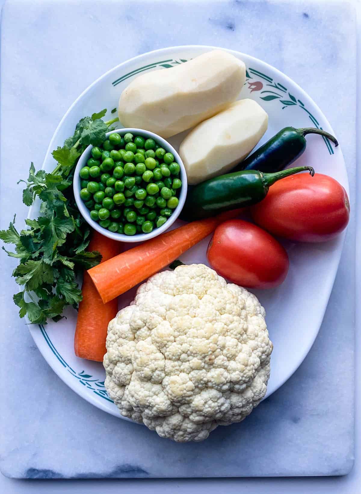Cauliflower, peas, potatoes and other vegetables  for Indian recipe on a white platter