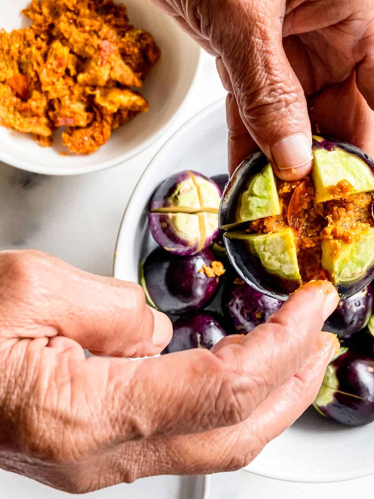 Hands stuffing baby eggplants with Indian spice mixture for stuffed eggplant recipe