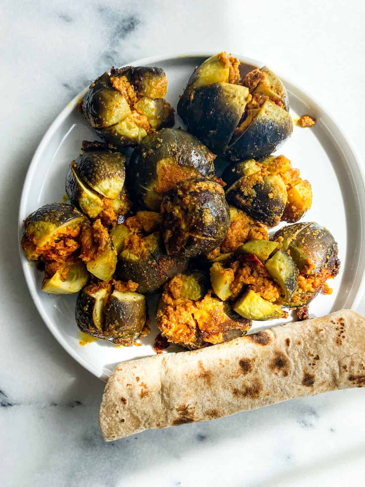 Stuffed Indian eggplants (Bharwa Baingan) served with Indian roti on a white plate