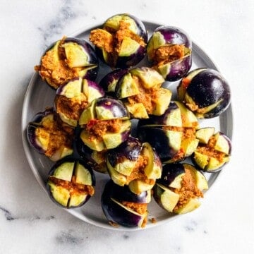 Uncooked stuffed baby eggplants (Bharwa Baingan) arranged on a white plate