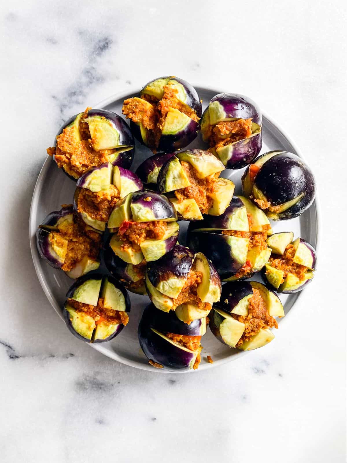 Uncooked stuffed baby eggplants (Bharwa Baingan) arranged on a white plate