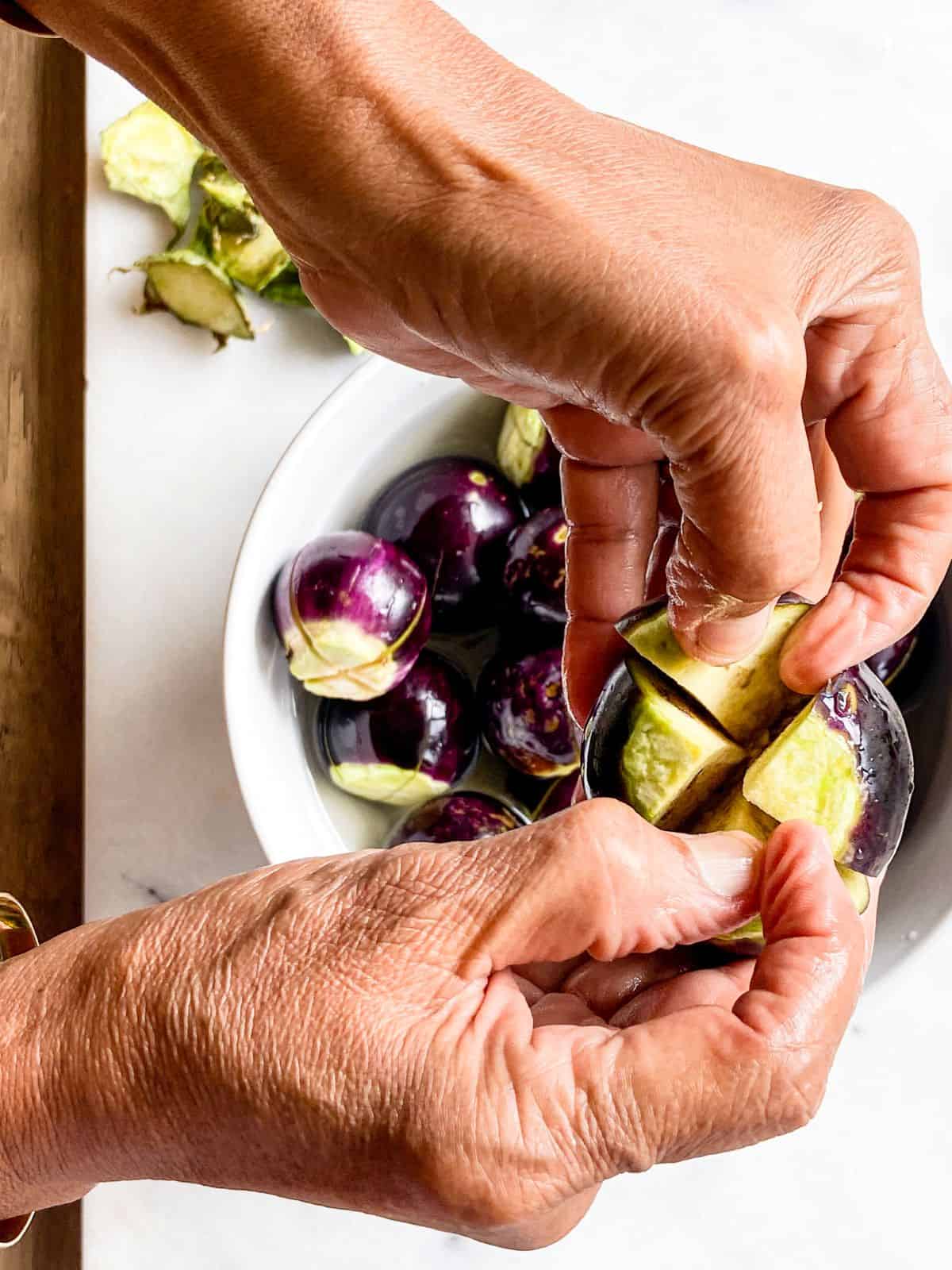 Hand holding a sliced baby eggplant showing how to cut it for stuffing