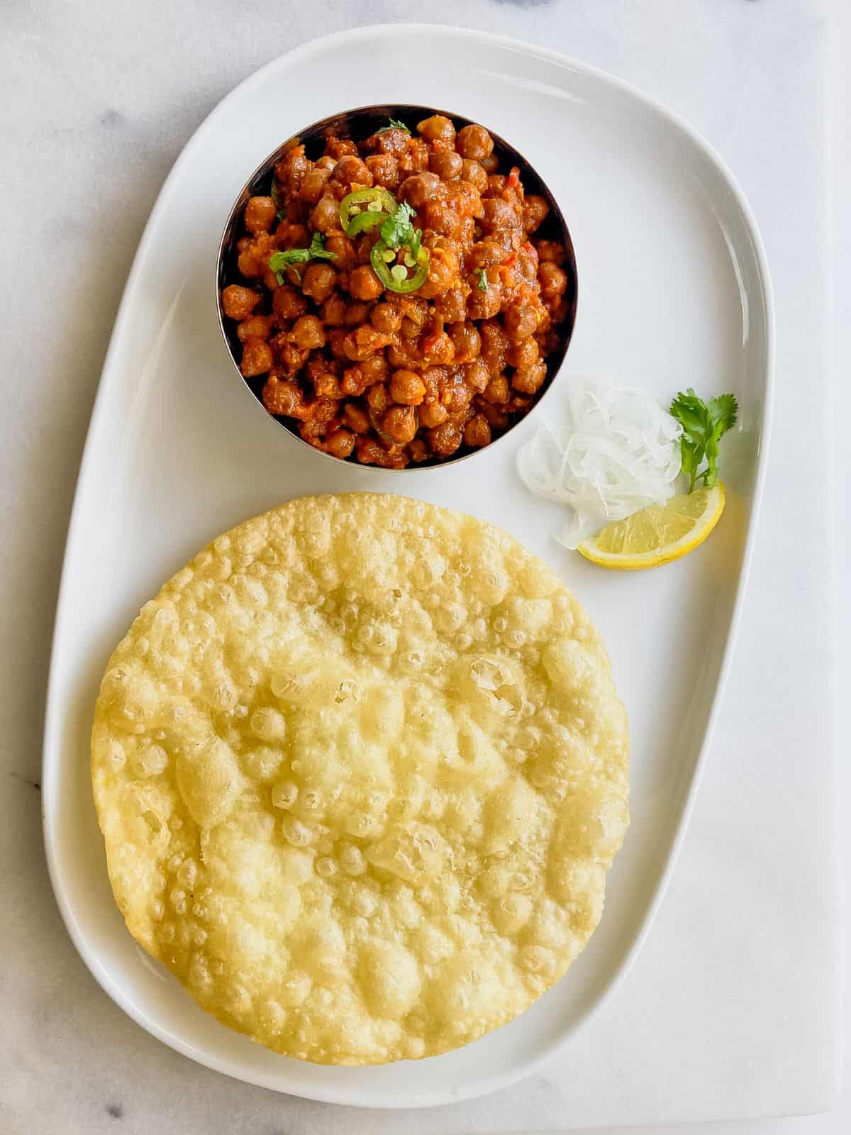 kala chana masala served with puri and sliced onion and lemon wedge
