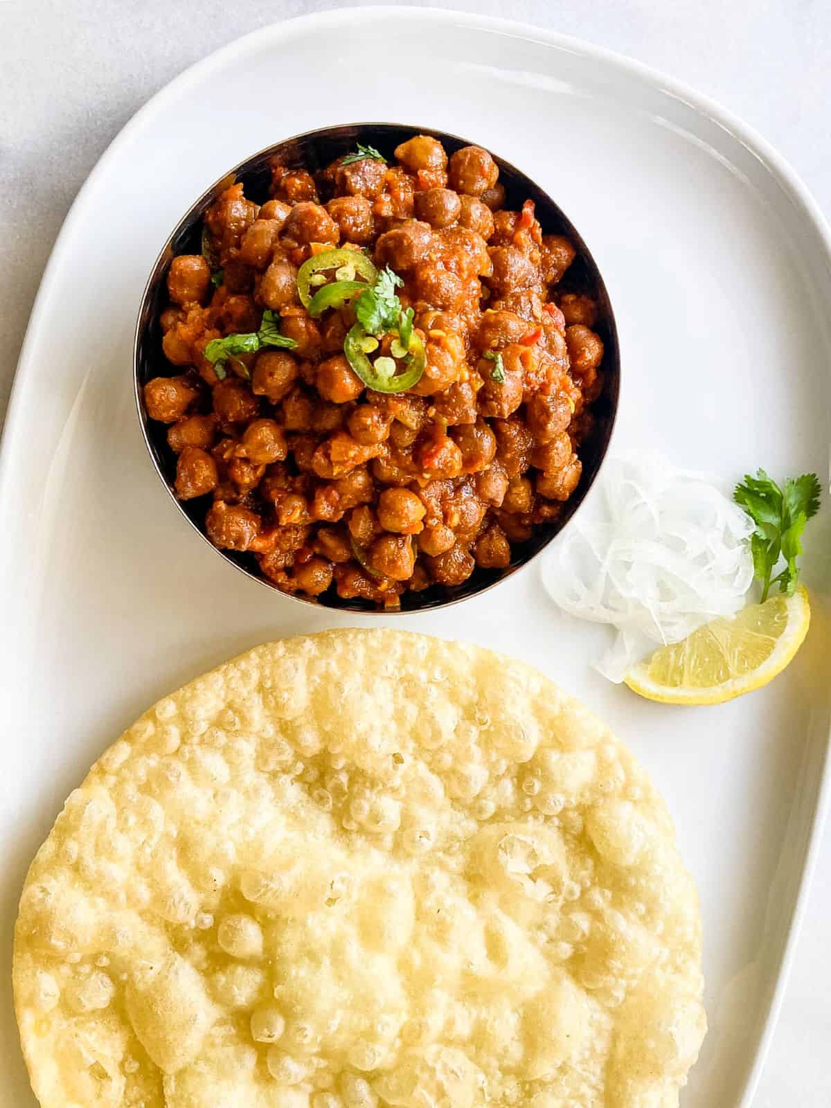 kala chana masala black chickpea curry with puri, sliced onion and lemon wedge