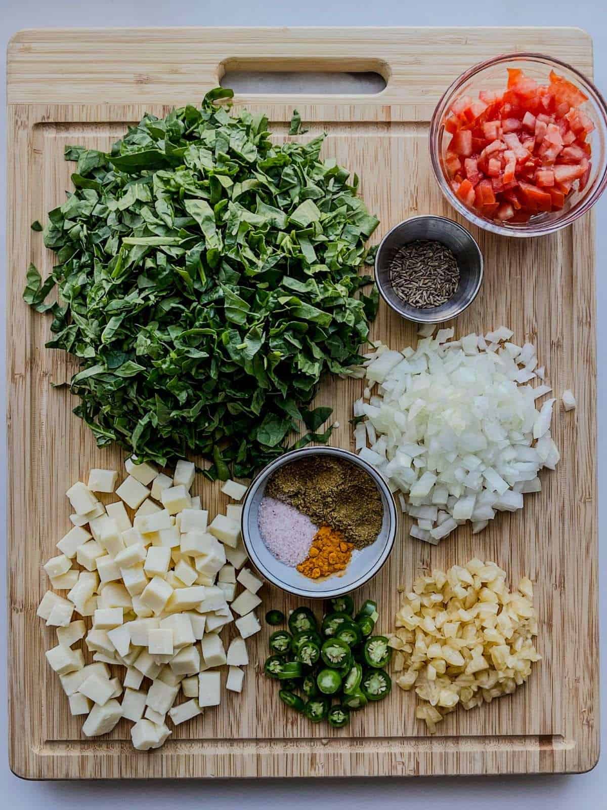 Ingredients for palak paneer stir fry including spinach, paneer, tomato, onion, garlic, chili and spices